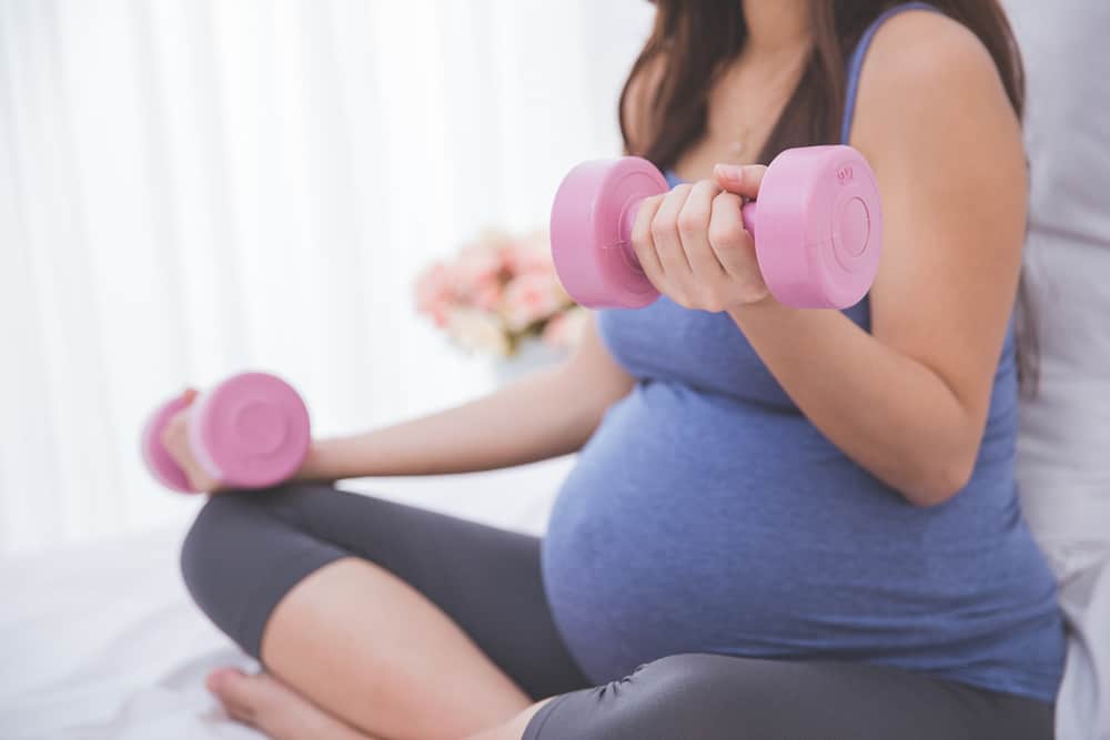 A portrait of a Beautiful asian pregnant woman doing exercise on her bed using dumbell