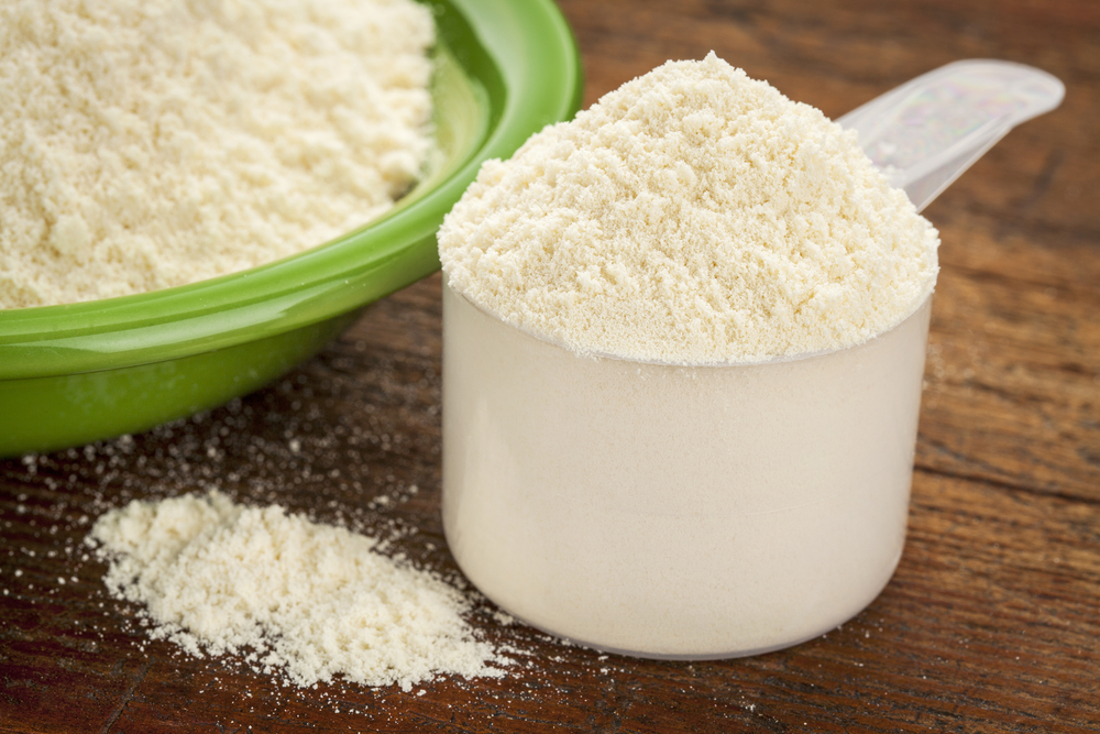 measuring scoop of whey protein powder with a bowl on wooden surface