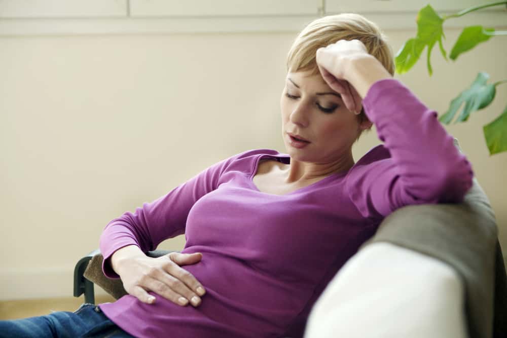 A woman sitting on a couch, clutching her stomach in